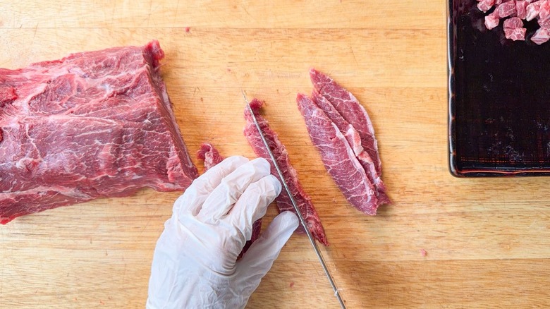 Cutting slices of raw flatiron steak into matchsticks on cutting board