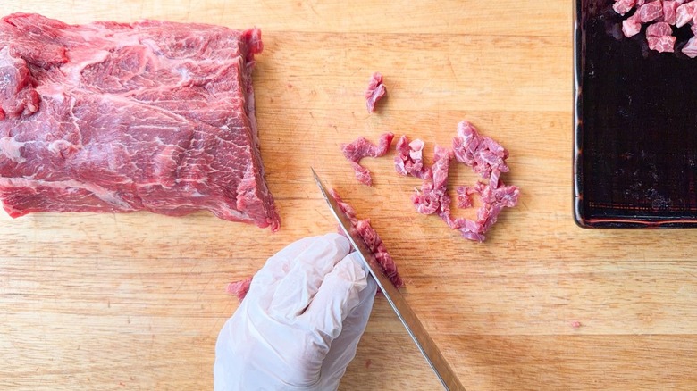 Cutting sliced raw flatiron steak into small cubes
