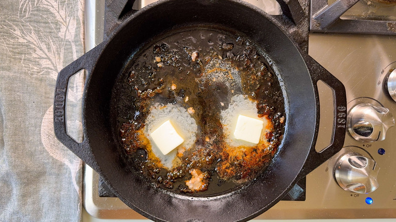 Butter melting with pork drippings in cast iron skillet on stovetop