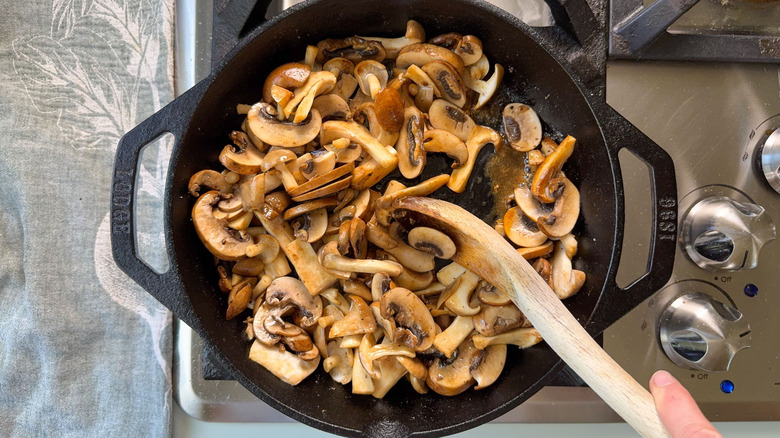 Stirring mushrooms with wooden spoon in cast iron skillet on stovetop