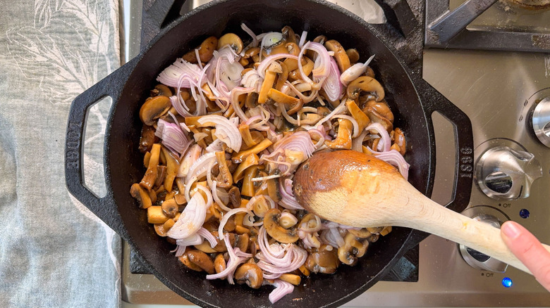 Stirring shallots and mushrooms with wooden spoon in cast iron skillet on stovetop