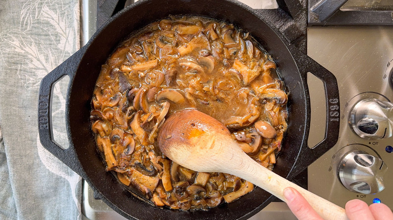 Stirring aromatic smothered pork chop sauce with wooden spoon in cast iron skillet on stovetop