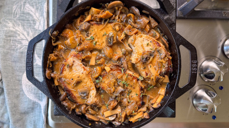 Aromatic smothered pork chops in cast iron skillet on stovetop