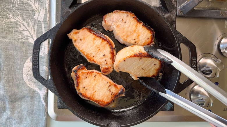 Browning pork chops in cast iron skillet on stove top and turning with tongs