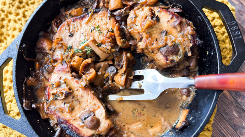 Aromatic smothered pork chops in cast iron skillet with metal spatula