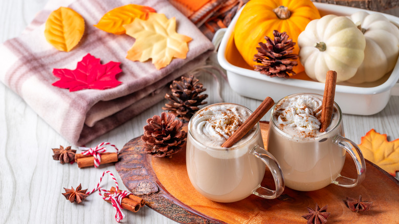 Two cups of pumpkin spice latte surrounded by pumpkins and fall decor