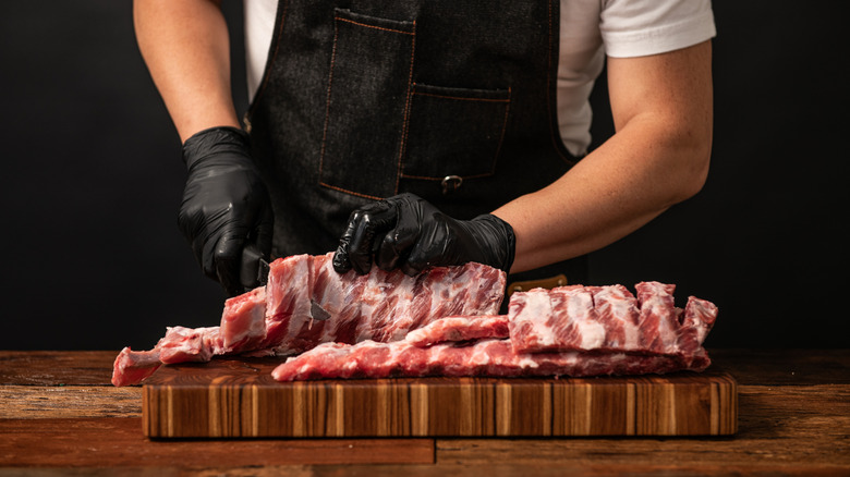 A butcher's hands are seen preparing ribs on a cutting board.
