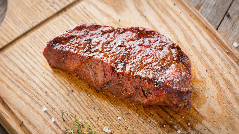 Cooked Denver steak on a cutting board with seasonings and herbs