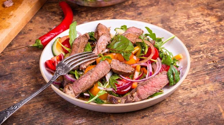 Sliced medium-rare steak on top of a salad with greens, onions, and tomatoes