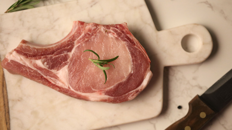 A pork rib chop is photographed on a white marble cutting board.