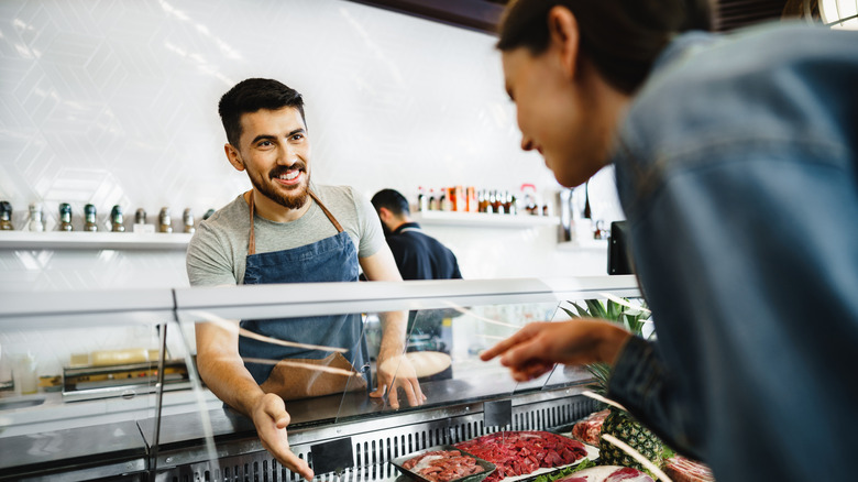 A person picks out meat from a butcher.