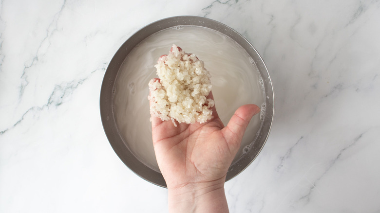 Hand holding rice above bowl of water