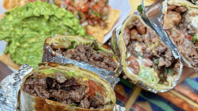 Two burritos sliced in half with chips and guacamole in the background