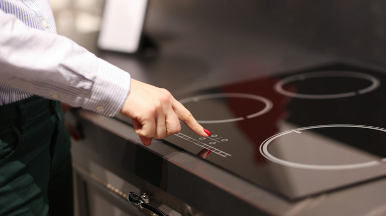 Person with red fingernails pressing a button on an electric cooktop