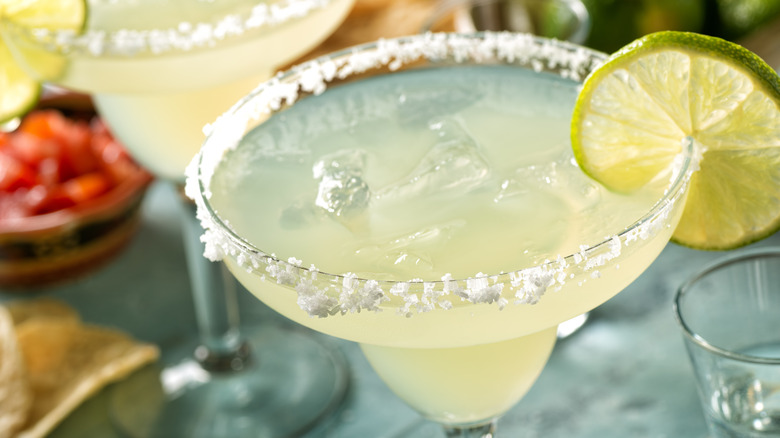 A freshly made margarita in a glass with a salted rim and lime wedge.