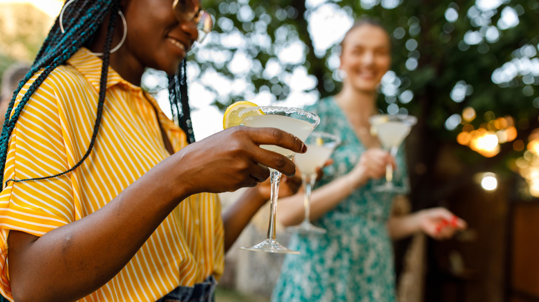 Two young women holding margaritas at an afternoon outdoor party.