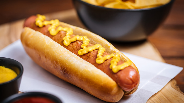 Hot dog on a bun with mustard on a napkin on a wooden table