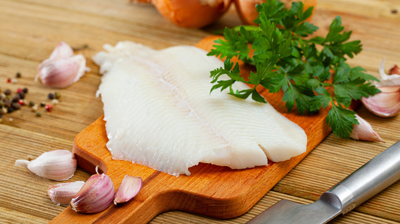 Atlantic halibut fillets on a wooden board surrounded by seasonings.
