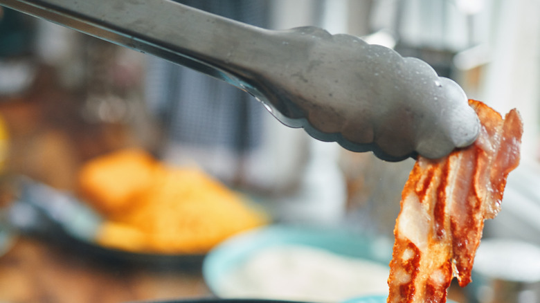 Tongs holding bacon strip