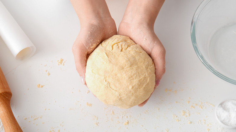 Hands with bread dough on white table