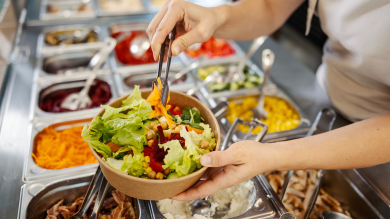 Person filling a bowl with salad ingredients at a buffet