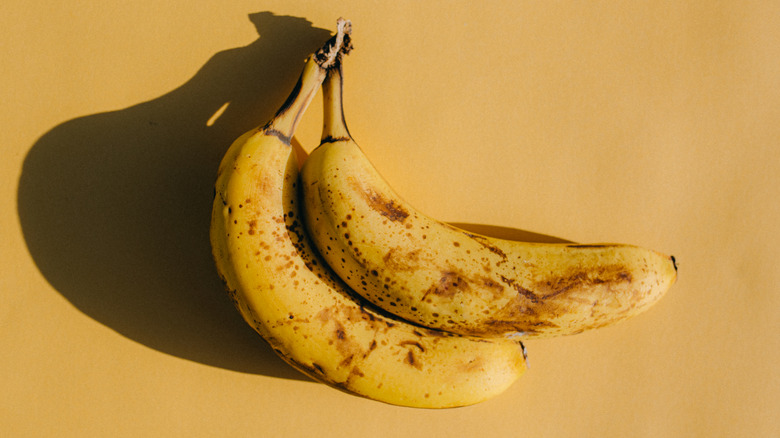 two ripe bananas rest on a yellow surface, casting a distinct shadow to the side