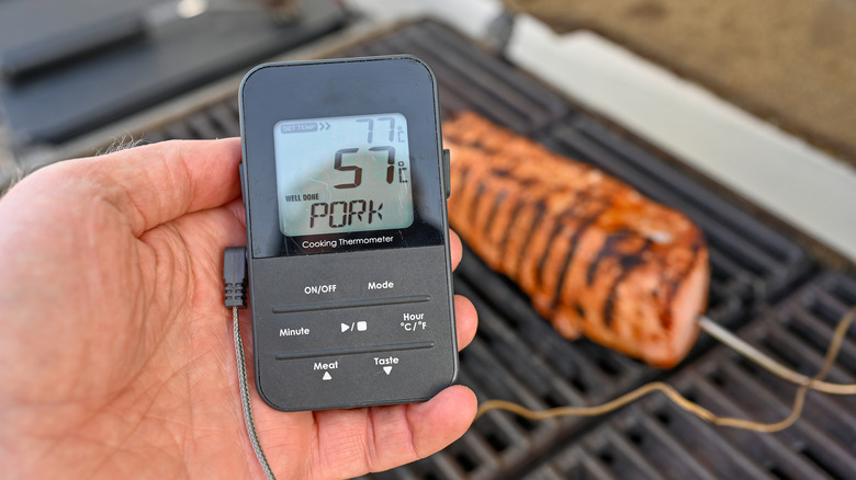 man holding bluetooth thermometers in pork on grill