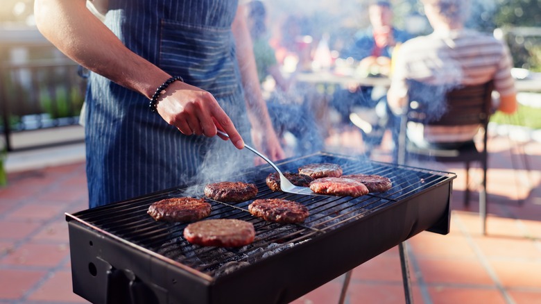 man in apron cooking burgers on a grill