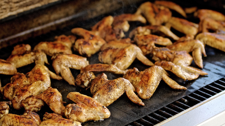 chickens wings on a barbecue with a grill mat underneath