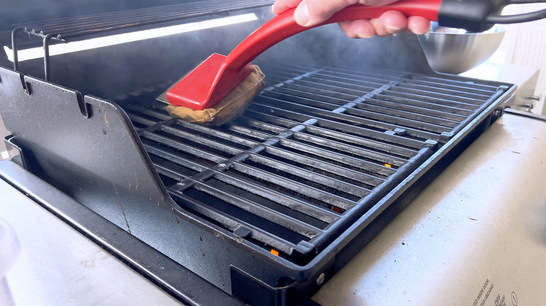 a person using a red grill brush to clean a grill