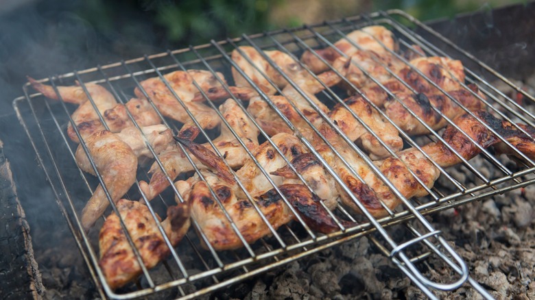 chicken wings inside a rotisserie basket over a grill