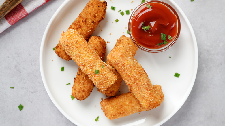 Mozzarella sticks on a white plate with dipping sauce