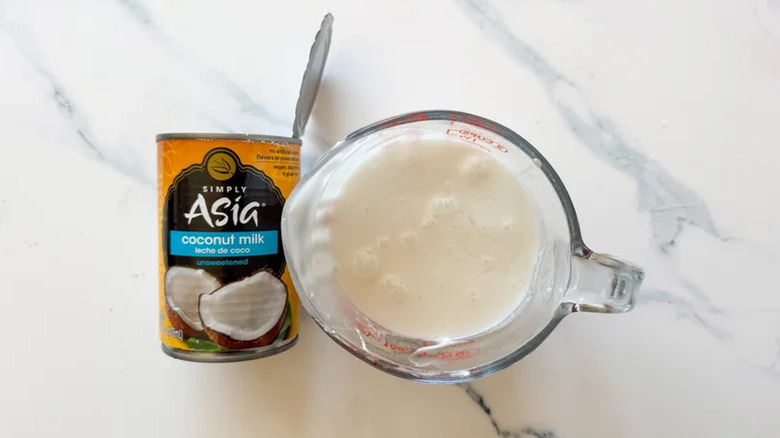 Open can of Simply Asia coconut milk next to a measuring cup of coconut milk on the counter