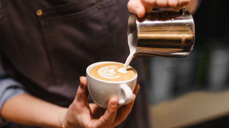 A barista pours frothy milk into a cup of coffee