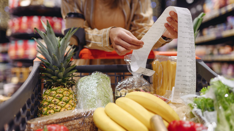 Close up of ﻿﻿fruit and vegetables in a shopping trolley with someone holding a long receipt