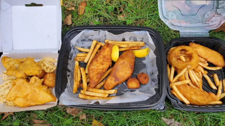 Three fish platters in to-go boxes on a grassy background