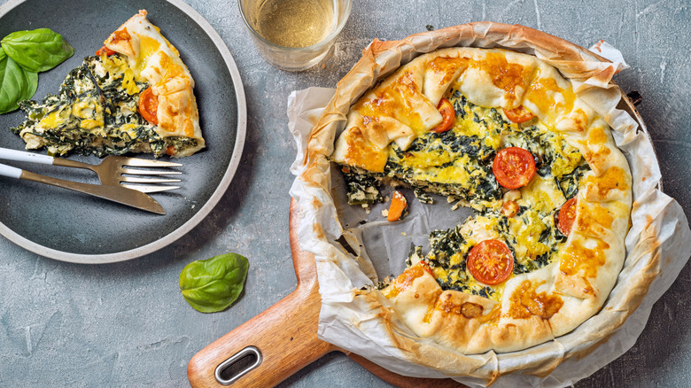 Slice of tomato and spinach quiche next to a pan of quiche