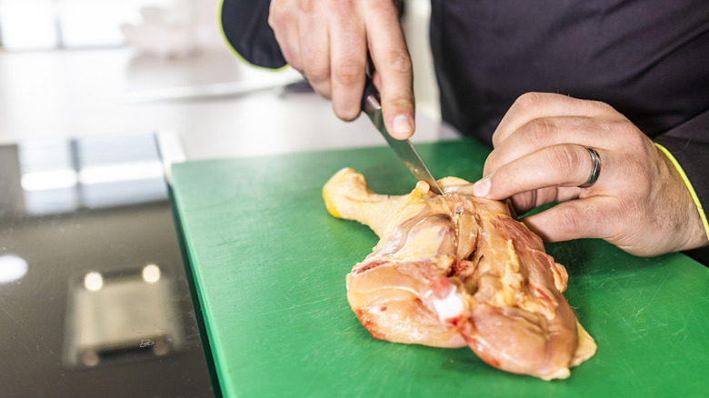 Person using a boning knife on raw chicken