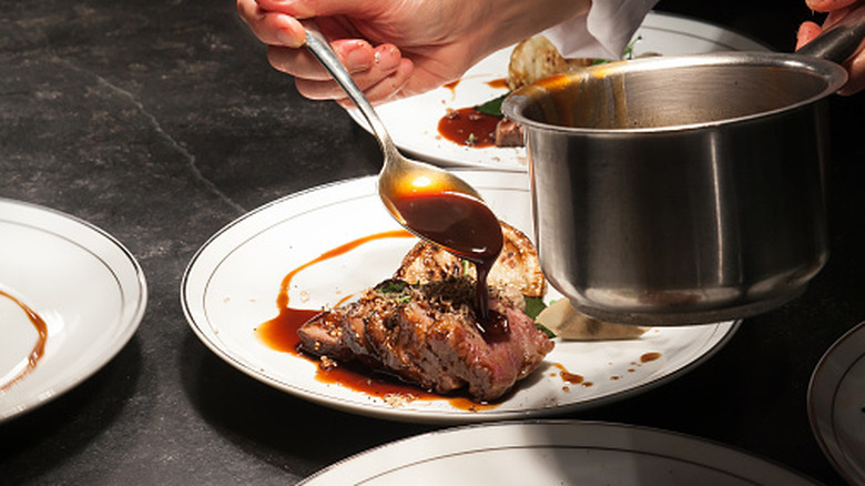 A chef pouring sauce over braised beef