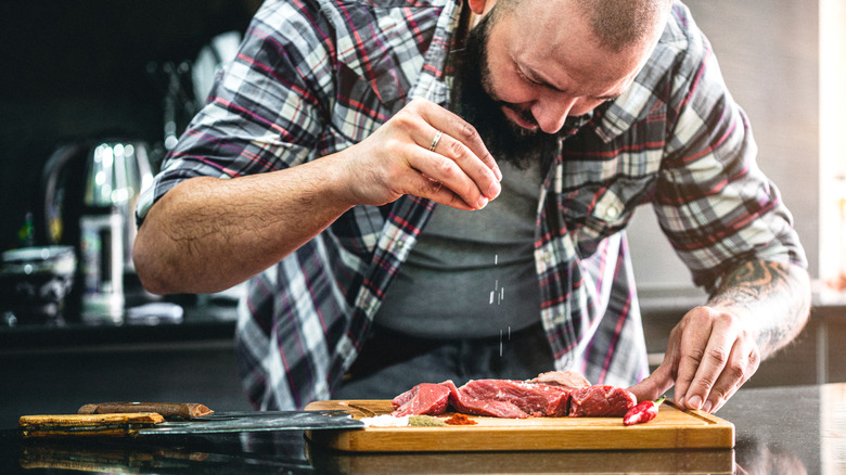 Middle age man seasoning beef on a cutting board with salt