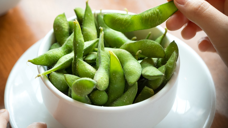 Hand taking edamame out of a white bowl