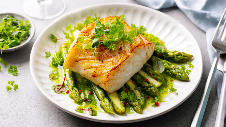 Fried cod with asparagus on a plate.