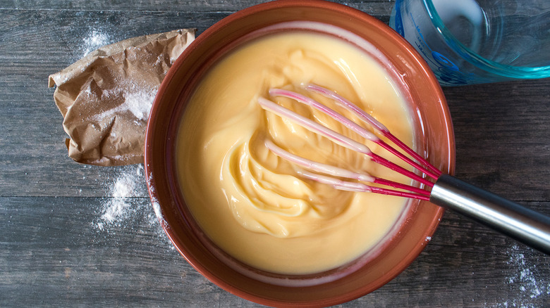 A red whisk in a bowl of vanilla pudding