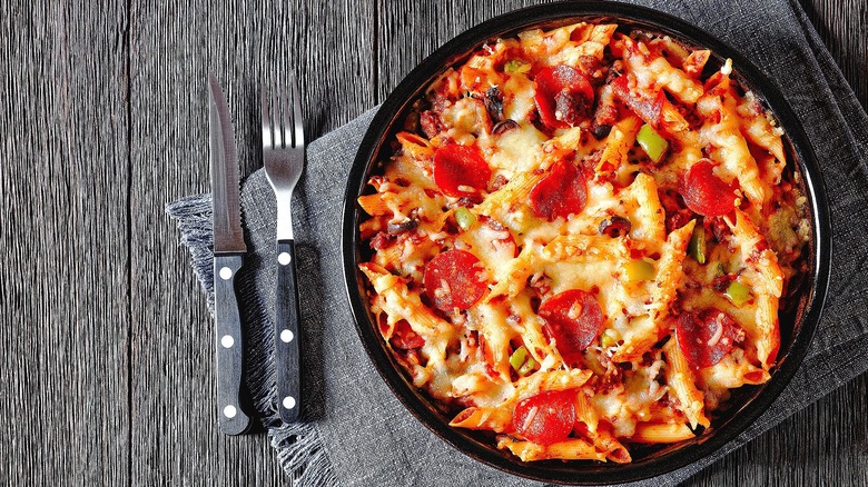 Pizza casserole with penne pasta, melted mozzarella cheese, and pepperoni slices in a black serving dish over a gray cloth napkin