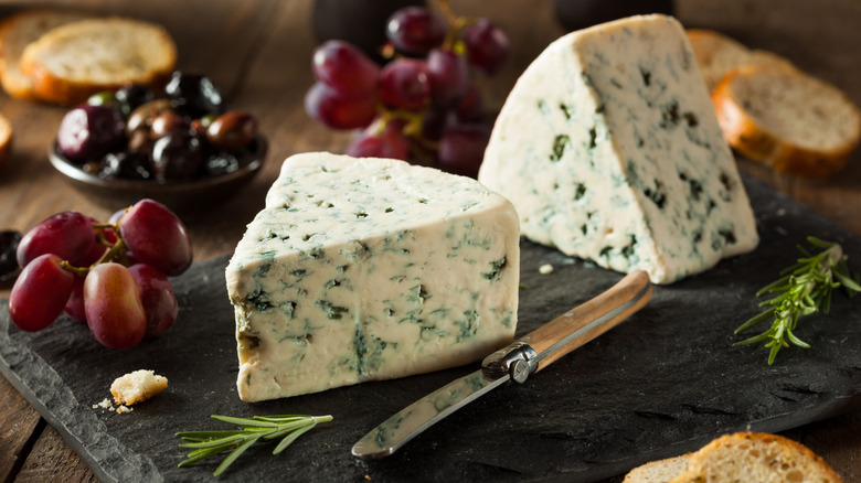 Wedges of blue cheese with grapes and a cheese knife on a wooden cutting board