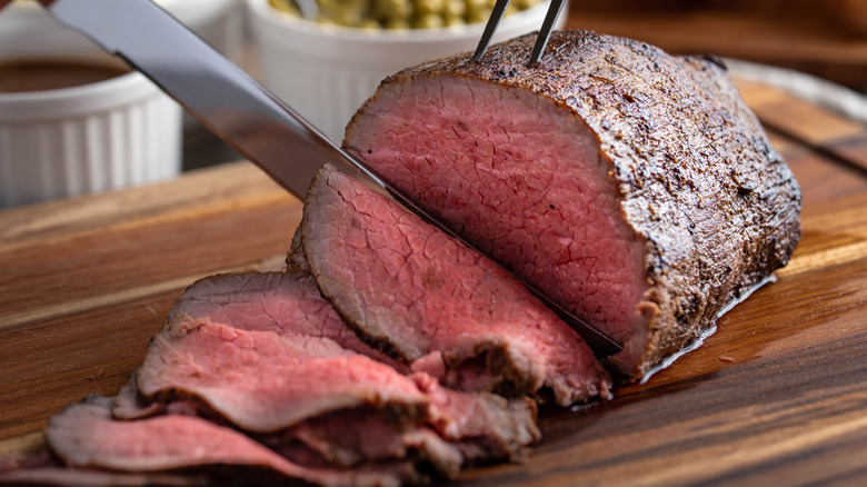 A person slicing roast beef on a cutting board