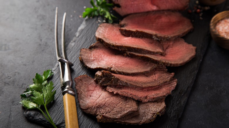 Slices of roast beef on a cutting board with a carving fork