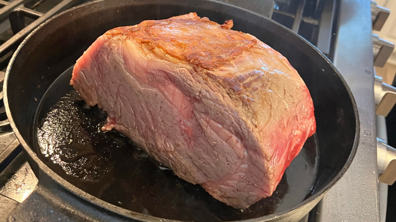 A piece of roast beef searing in a pan