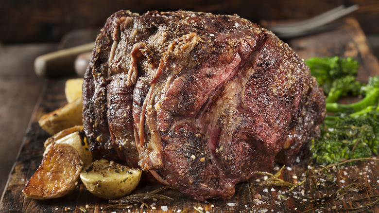 A whole beef roast on a cutting board with potatoes