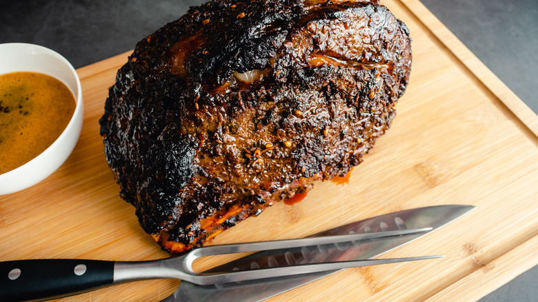 A roast beef with a carving knife and fork sitting on a wooden cutting board